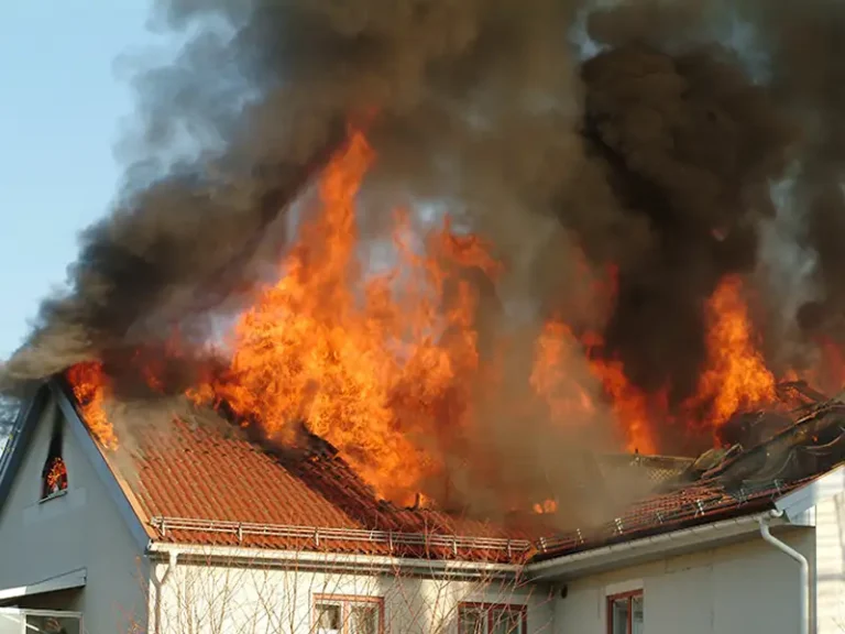 Fire engulfing the roof of a house with thick black smoke rising into the sky.