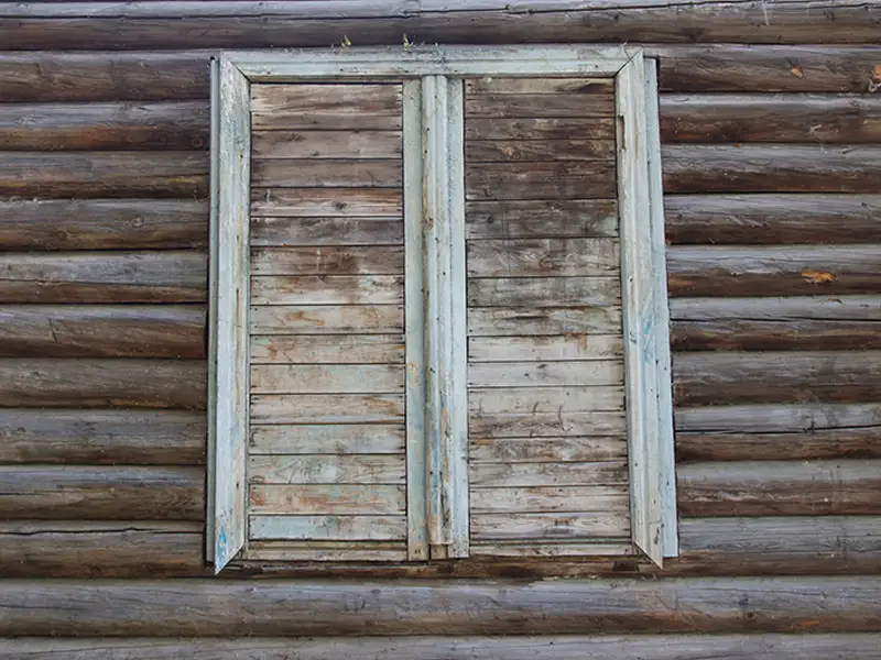 Closed weathered wooden shutters on a log cabin wall.