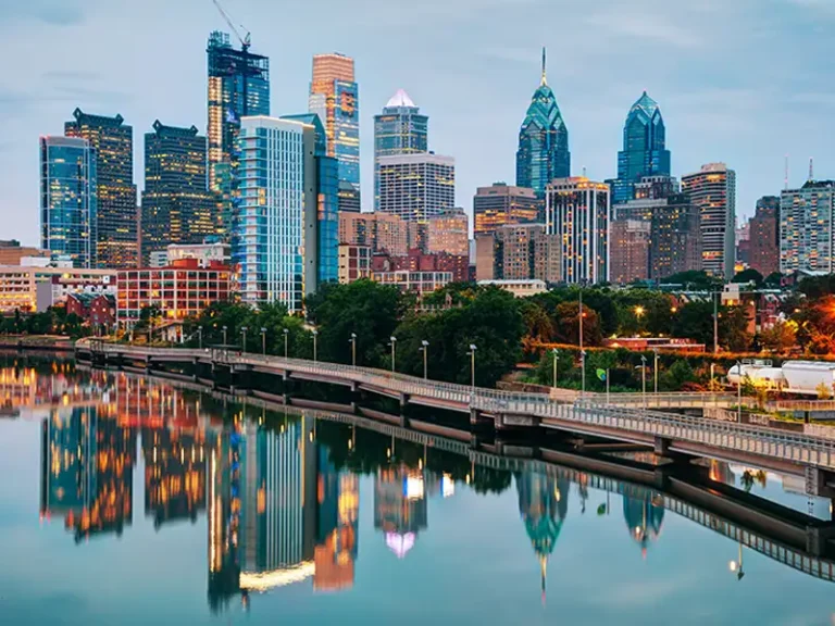 Philadelphia skyline with skyscrapers reflecting in a calm river at dusk.
