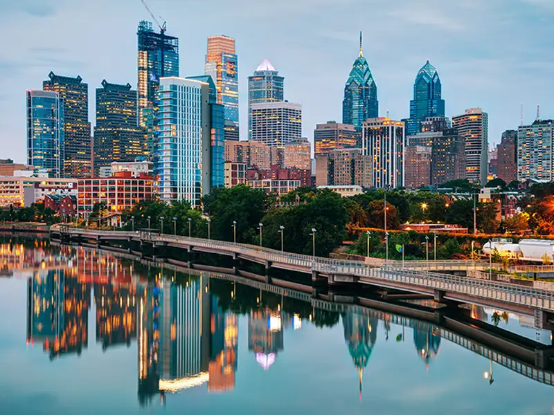 Philadelphia skyline with skyscrapers reflecting in a calm river at dusk.