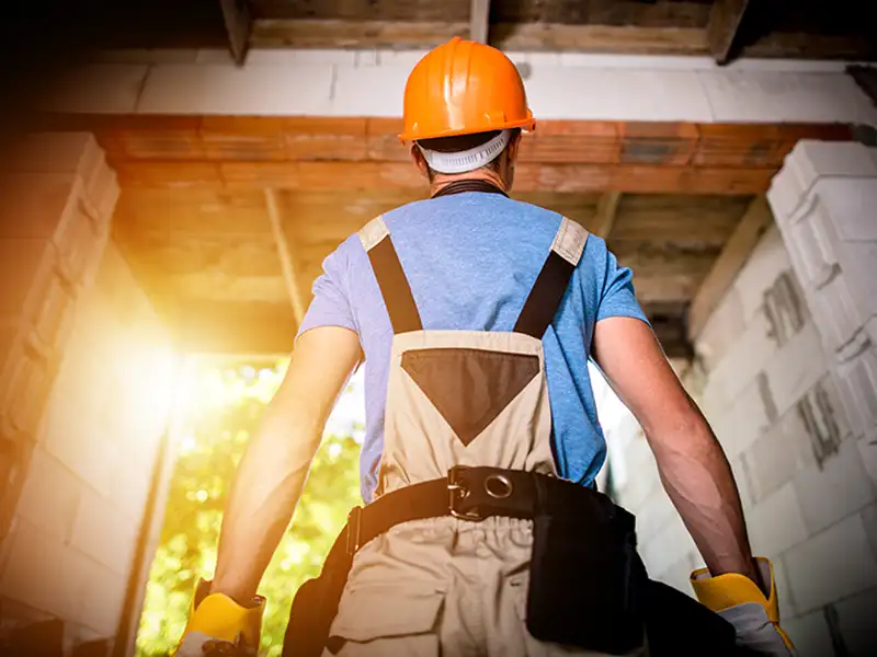 Construction worker wearing an orange helmet and gloves inside a building under construction.