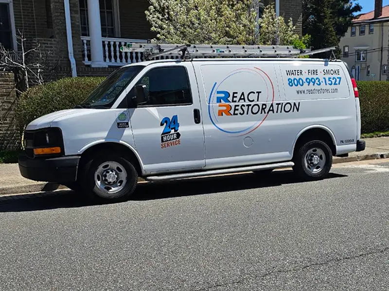 White service van with ladder on top and "React Restoration" signage parked on a street.