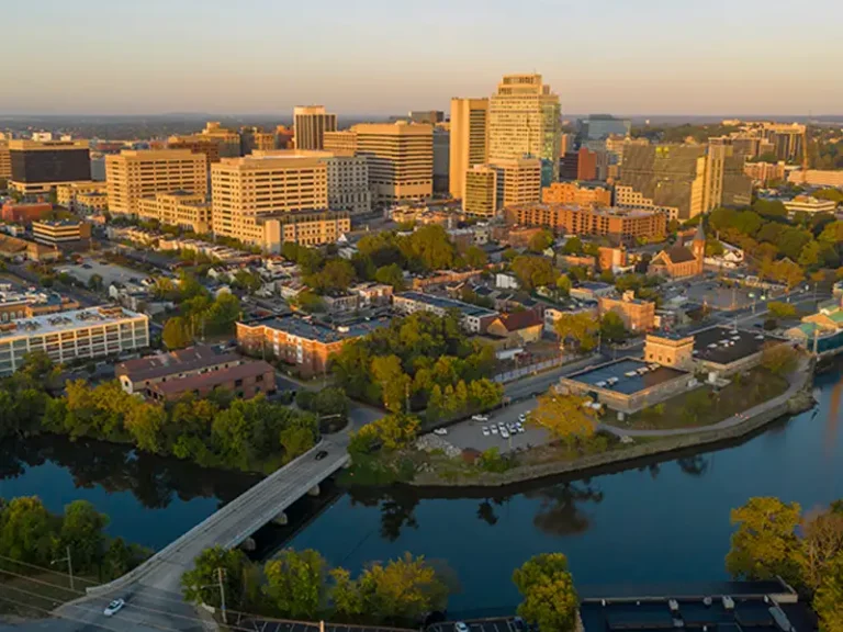 Downtown cityscape with buildings and a river crossed by a bridge at sunset.