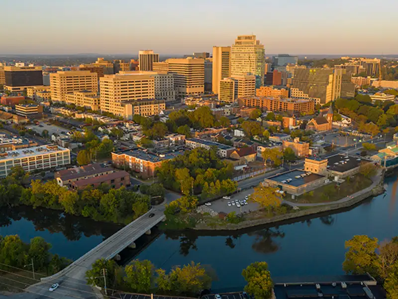 Downtown cityscape with buildings and a river crossed by a bridge at sunset.