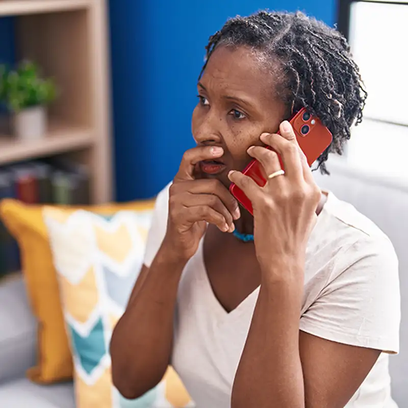 Worried woman with short dreadlocks talks on a red phone indoors.